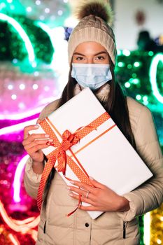 Vertical Shot of portrait beautiful female in mask standing on street. Young woman with christmas present. Winter concept.