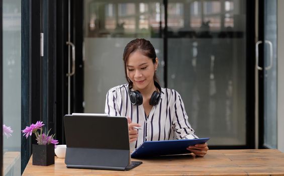 Smiling Asian young female using headset looking at laptop screen listen and learning online courses. Happy chinese business woman with headphones video call for customer service.