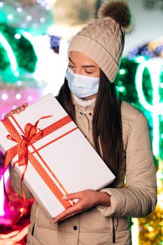 Portrait beautiful female in mask standing on street. Young woman with christmas present. Winter concept.