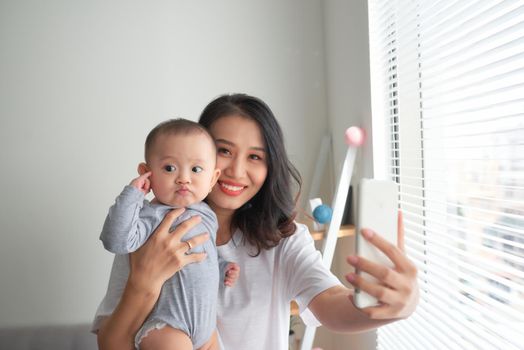 Young mother is making selfie with her adorable little baby and smiling