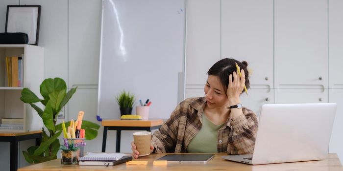 Portrait of cheerful asian woman with casual life with morning coffee and sitting on chair in home office. Concept of young business people working at home