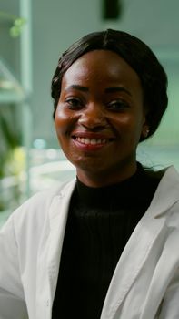 Portrait of biologist researcher woman in white coat looking into camera while standing in microbiology laboratory. Specialists team researching genetic mutation developing medical scientific GMO dna test