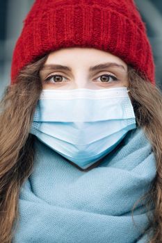 Close up portrait of Caucasian young curly female in medical mask standing in winter city. Crowd people sick covid-19. Epidemic coronavirus. Pandemic flu corona virus.