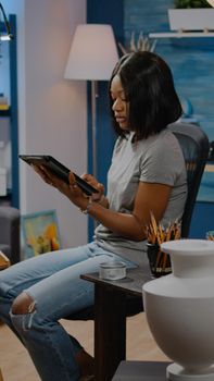 Black young artist holding digital tablet for vase drawing in artwork studio. African american woman using modern technology seeking inspiration for next masterpiece project on canvas