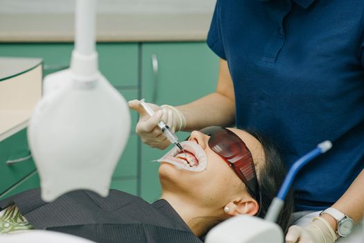 Dentist stomatologist whitening teeth for patient. Application of protective whitening gel to the teeth. Woman with an expander in mouth at the dental clinic. Beautiful smile. The health of teeth.