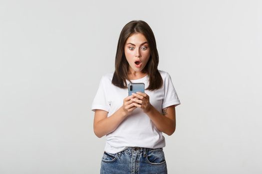 Shocked and impressed brunette girl looking amazed at smartphone screen.