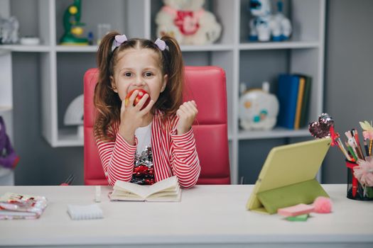 Cute little girl eating an apple while learning online lessons. Portrait of a little girl eating apples