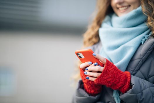 Female fingers tapping on cellphone outdoors. Modern holidays online shopping, buying new year's gifts. Close up of woman hands texting on smartphone standing on street in winter city on New Year.