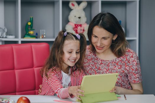 Mother and daughter doing homework online. Distance learning online education. Schoolgirl with digital tablet laptop notebook and doing school homework. Mom does homework with her daughter at home