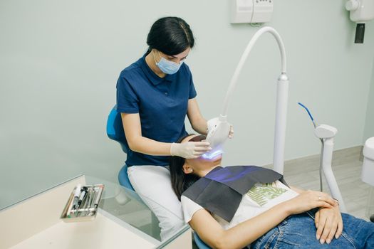 Teeth whitening procedure. Dentist stomatologist whitening teeth for patient in medicine dental clinic with lamp. Concept of teeth care and dentistry.