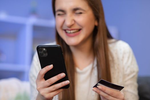 Cheerful female using mobile phone while doing online payment with bank card on purple background