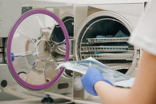 Medical Sterilizer Interior. Medical autoclave for sterilising surgical and other instruments. Young Female Dentist Places Medical Autoclave For Sterilising Surgical And Other Instruments