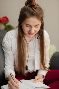 Smiling teen girl wearing headphones listening to audio course making notes, young woman learning foreign languages, digital self education, studying online, enjoying music