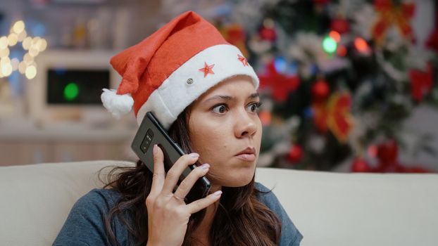 Close up of stressed person talking on smartphone for business meeting. Irritated woman with santa hat using phone call for work on christmas eve. Adult working on winter holiday