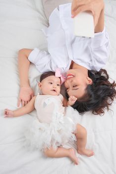 Smiley mother and her baby looking at you lying on the floor at home