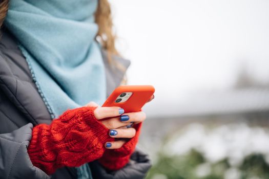 Close up of woman hands texting on smartphone standing on street in winter city on New Year. Female fingers tapping on cellphone outdoors. Modern holidays online shopping, buying new year's gifts.