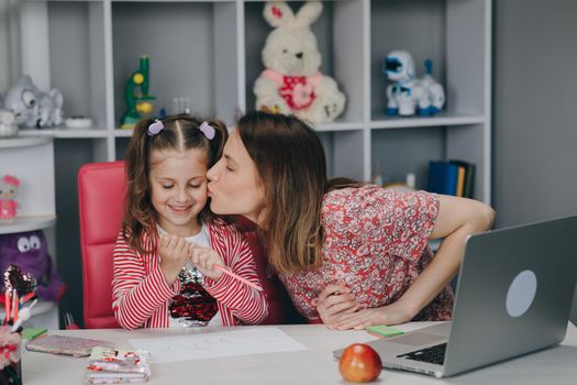 Distance learning online education. Schoolgirl with laptop notebook and doing school homework. Mom does homework with her daughter at home.