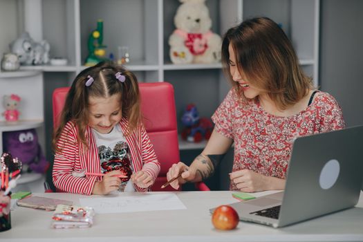 Young mother looking how her daughter drawing a picture. Mother and her child drawing.