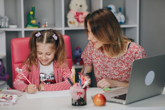 Mother and kid at home doing homework online. Distance learning online education. Mom does homework with her daughter at home.