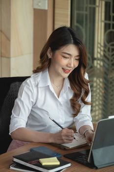 Portrait charming asian woman taking note on notepad while video conference via digital tablet.