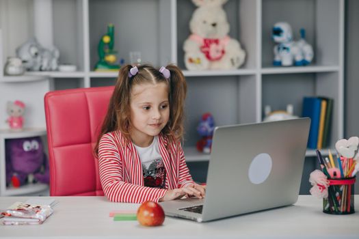 Pretty girl distance learning at home. Focused cute kid listening audio lesson studying at table, doing homework. Children remote education on quarantine concept.