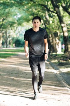 Adult man running outdoor using wireless bluetooth earphones listening to music with smartwatch enjoying healthy. Male runner working out cardio exercise workout in city park.