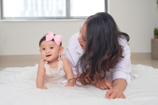 Smiley mother and her baby looking at you lying on the floor at home