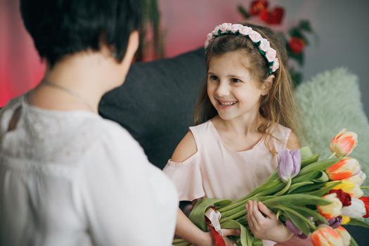 Little daughter congratulates her elderly mother on Mother's Day. A little girl hugs her mom. Happy Mother's Day.