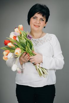 Woman with tulip bouquet. Woman with gifts. Attractive woman holds bouquet of flowers tulips in her hands gift soft toy looking at camera and smiling