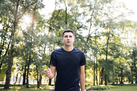 Male person running along the road in the city park. Urban business person training outside enjoying fresh nature. Healthy active lifestyle. Summer sunny morning. Distance sport app.