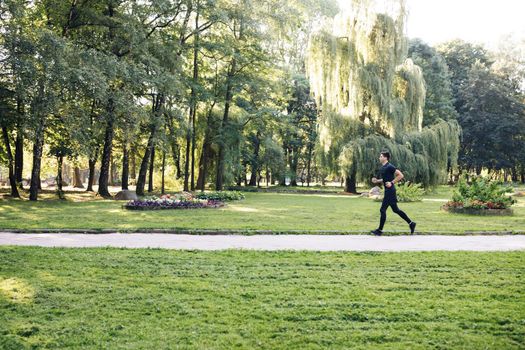 Man in summer sports uniform running in the city park with smartwatch for measuring speed, distance and heart rate. Wireless earphones. Training outside