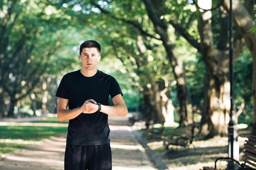 Adult man running outdoor using wireless bluetooth earphones listening to music with smartwatch enjoying healthy. Male runner working out cardio exercise workout in city park.