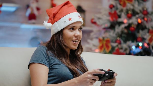 Woman playing video games with controller on tv console and feeling happy on christmas eve. Festive adult enjoying online play with joystick on television screen, having fun on holiday