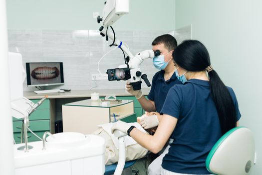 Medical Stomatology Concept. Doctor making teeth examination research survey using microscope in dentistry. Dentist is treating patient in modern dental office.