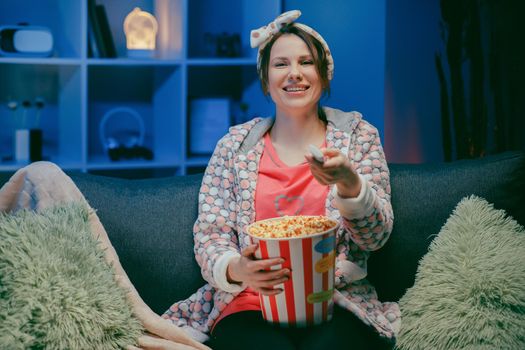 Cheerful casual young woman with funny face eating popcorn and looking film sit on sofa enjoy sincere positive emotions screaming with laughter concept