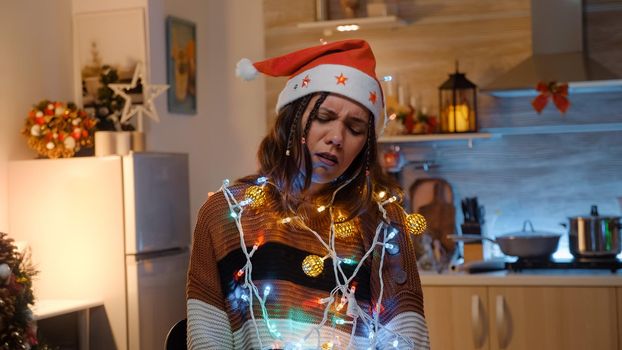 Young adult with knotted string of christmas lights tangled while trying to decorate home for winter holiday. Festive woman preparing for dinner party celebration with friends and family
