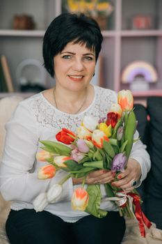 Woman holding tulips and smiling to the camera. Beautiful Woman In Nice Spring Bouquet Of Tulips. Woman showing a bunch of assorted flowers. Smiling woman with bunch of flowers.