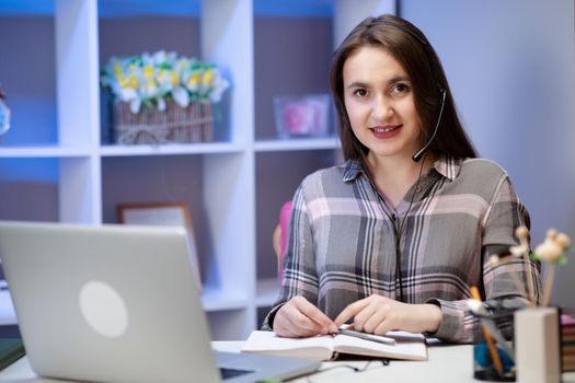 Positive charming woman working at home. Smiling young woman student wear headset using laptop for e learning course online teaching in internet at home.
