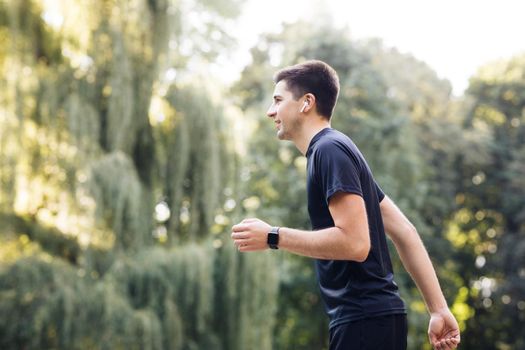 Handsome man using trendy earphones and smart watch. Sporty person training outside enjoying fresh nature. Healthy active lifestyle. Summer sunny day. Distance, heartbeat sport app.