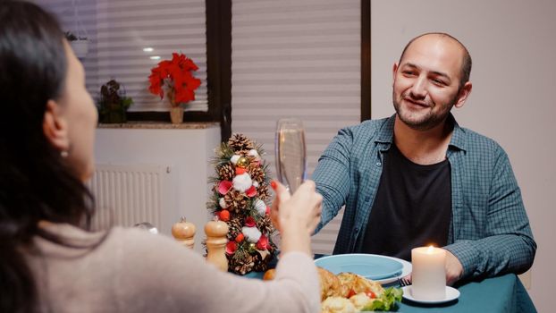 Close up of man clinking glasses of champagne with woman, celebrating christmas dinner. Couple enjoying meal, eating chicken and drinking alcohol on traditional holiday festivity.