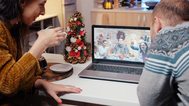 Festive couple talking to family on video call at christmas dinner. Man and woman using laptop for remote conference online, enjoying holiday celebration on internet. People speaking to relatives