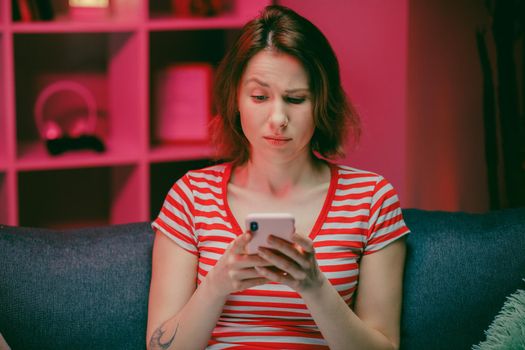 Happy Young Woman Holding Smart Phone Looking at Cellphone Screen Laughing Enjoying Using Mobile Apps for Shopping. Having Fun Playing Games Chatting in Social Media Sit on Couch at Home.