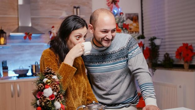 Man and woman waving at video call camera and talking to family, celebrating christmas eve on online remote conference. Festive couple chatting with relatives and enjoying festivity