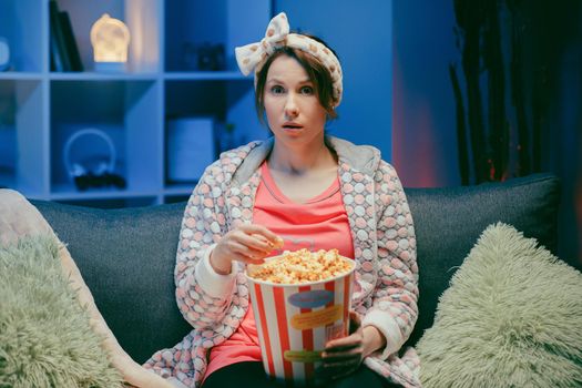 Woman watching TV laughing and eating popcorn having fun at home alone enjoying modern television. Youth lifestyle and cheerful people concept.
