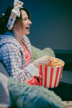 Woman watching funny movie on the tv and eating popcorn on sofa