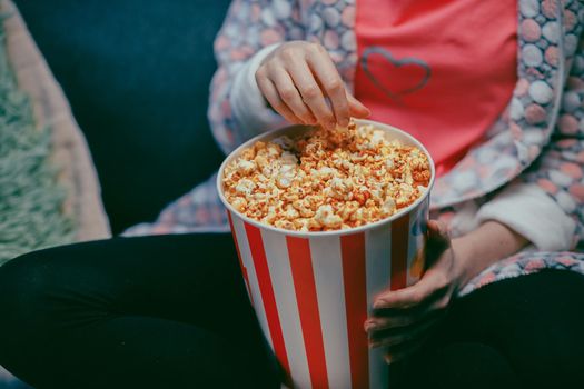 Female hand picking popcorn from paper bucket closeup. Close up of woman eating pop corn at cinema. Movie food concept. Female hand taking popcorn in bucket at cinema