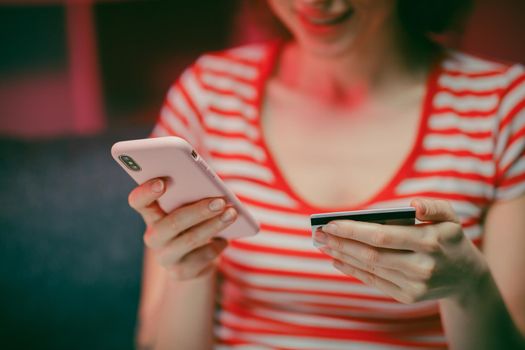 Close up Hand of young woman are buying online with a credit card while sitting on the sofa in the living room. Women are using smartphone and doing online transactions.