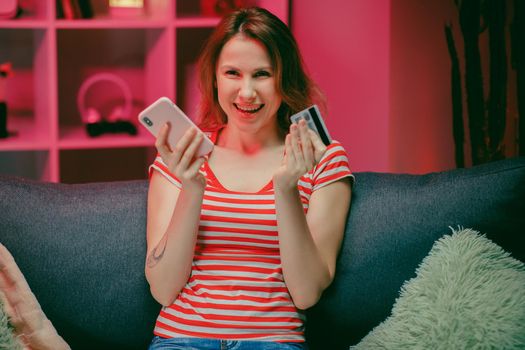 young woman are buying online with a credit card while sitting on the sofa in the living room. Women are using smartphone and doing online transactions.