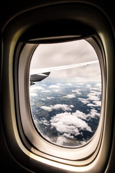 View looking out an airplane jet window on a calm sunny day with white clouds in a blue sky and land below making a beautiful travel background photograph image.