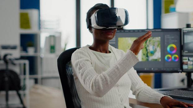 Black videographer wearing VR headset editing project in production studio office. Video maker employee processing film montage in digital multimedia company while, colleagues working in background